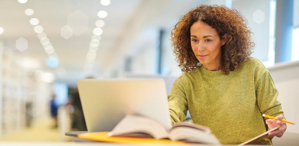 Woman sitting at a desk and looking at her laptop screen.