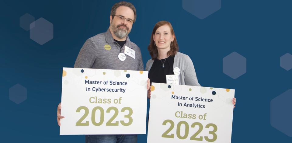 Man (left) smile and holding a sign that say "Master of Science in Cybersecurity Class of 2023" and woman (right) smile and holding a sign that say "Master of Science in Analytics Class of 2023."