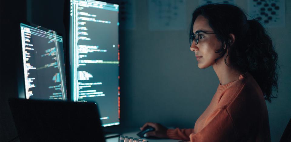 A woman sitting at a desk with multiple monitors.