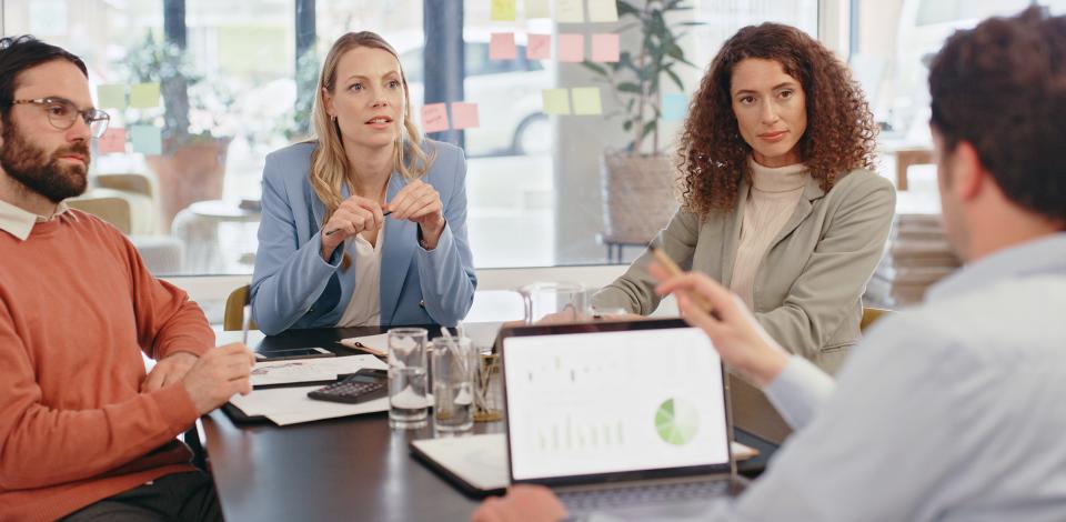 Four professionals sitting around a table discussing data on a laptop