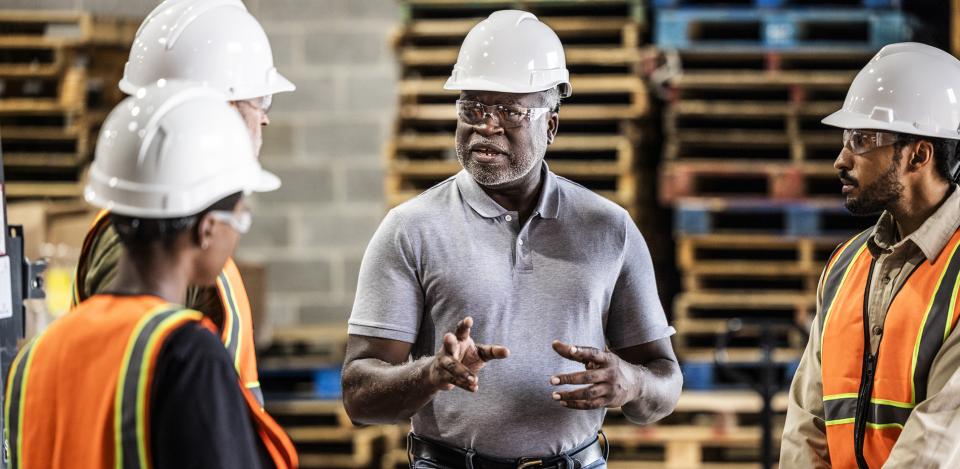 Safety officer in a hard hat speaking with employees in hard hats and other personal protective equipment