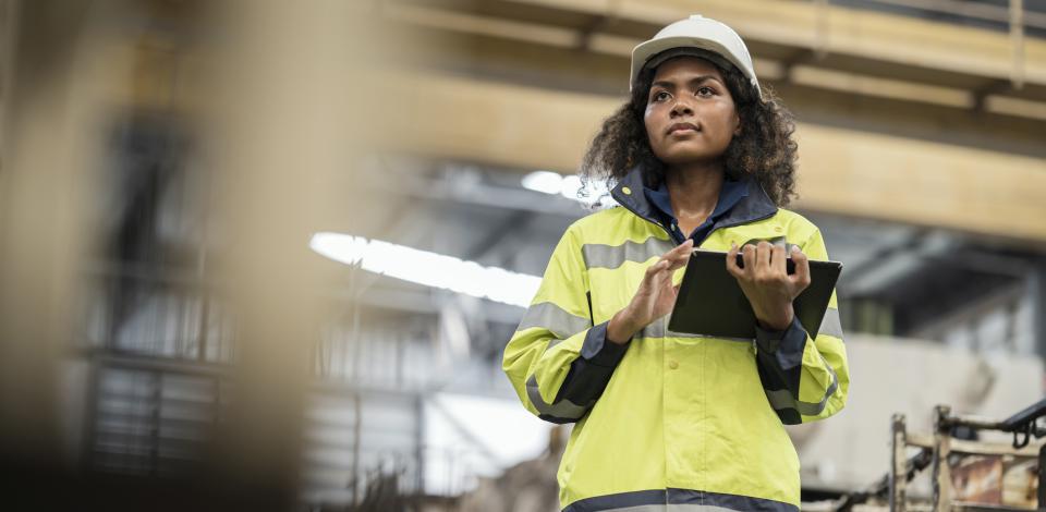 Woman in a hard hat and reflective coat walking through a warehouse