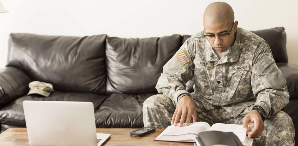 Soldier sitting on couch with books and laptop on table