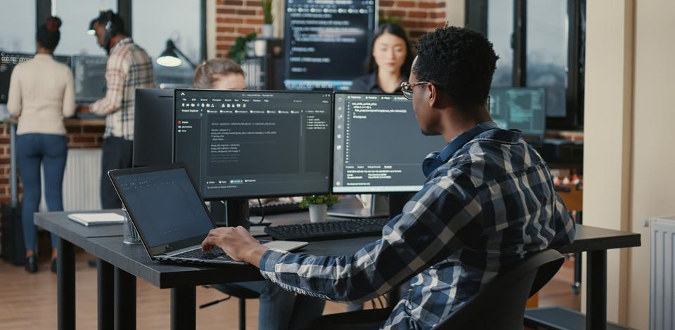 Person sitting at desk with multiple monitors, coding.