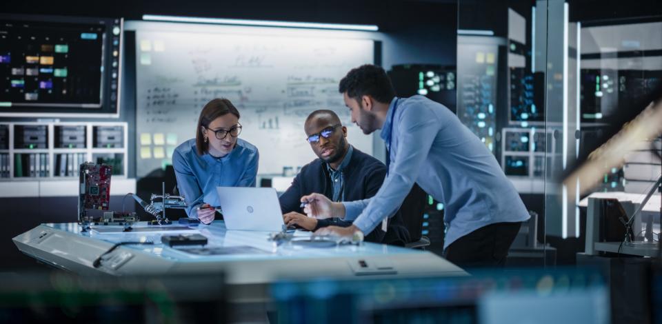 three people sitting at a desk discussing content on a lap top