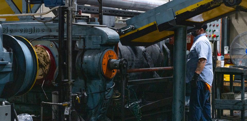 Worker inspecting a large industrial machine with gears and control panels.