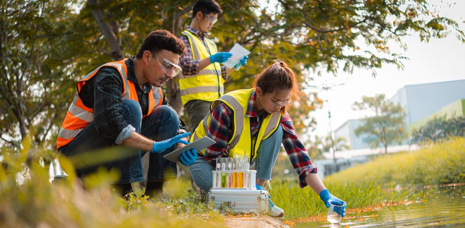 Three environmental health and safety specialists taking water samples outside of a manufacturing plant.