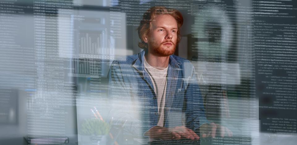 Man sitting at desk looking at floating lines of code and different charts meant to symbolize AI outputs