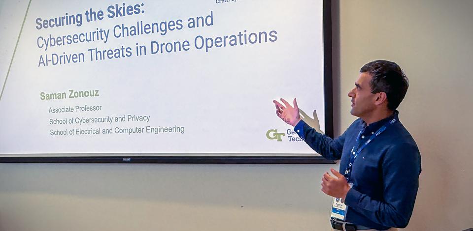 Photograph of a man giving a presentation titled "Securing the Skies: Cybersecurity Challenges and AI-Driven Threats in Drone Operations."
