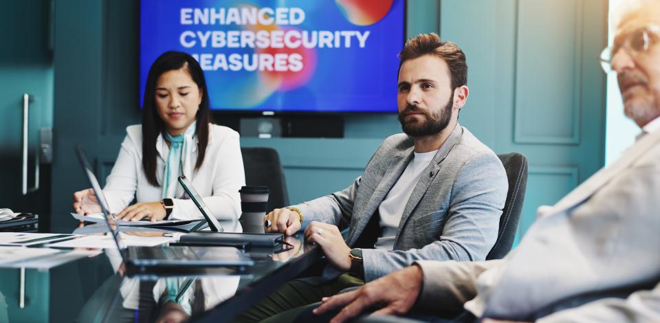 Three cybersecurity professionals sitting in a conference room giving a presentation on cybersecurity measures.