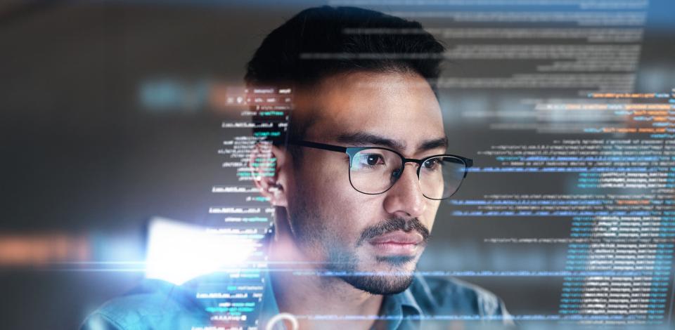 A man focused on a transparent screen displaying lines of computer code.