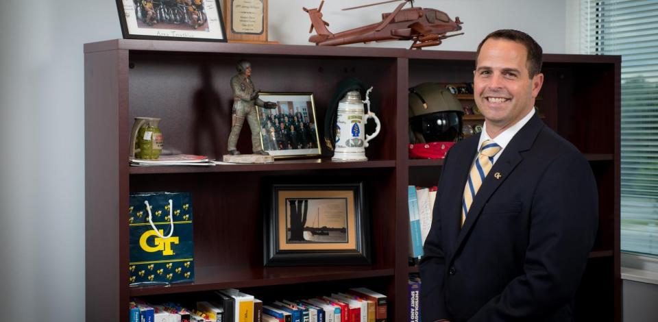 James Wilburn standing in front of bookshelf in his office with military memorabilia