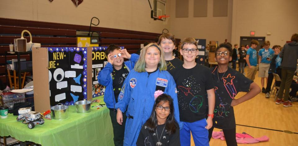 Lego League team poses for picture next to their project board and wearing space gear