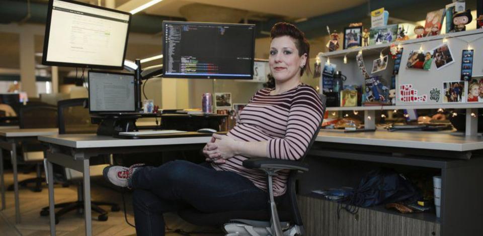 Coding Boot Camp graduate sitting in office chair in front of two desktop screens