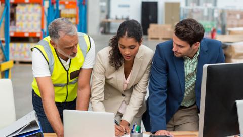 Three logistics professionals collaborating over computer in warehouse