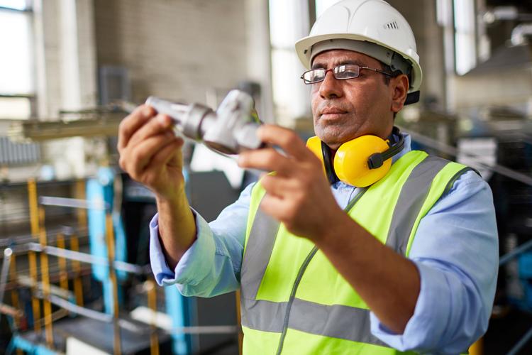 Manufacturing professional in safety gear inspecting a part 