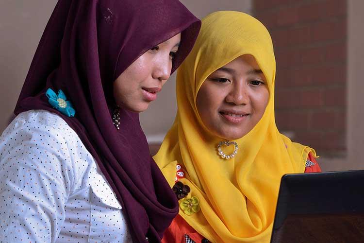 Two international women with head scarfs looking at laptop