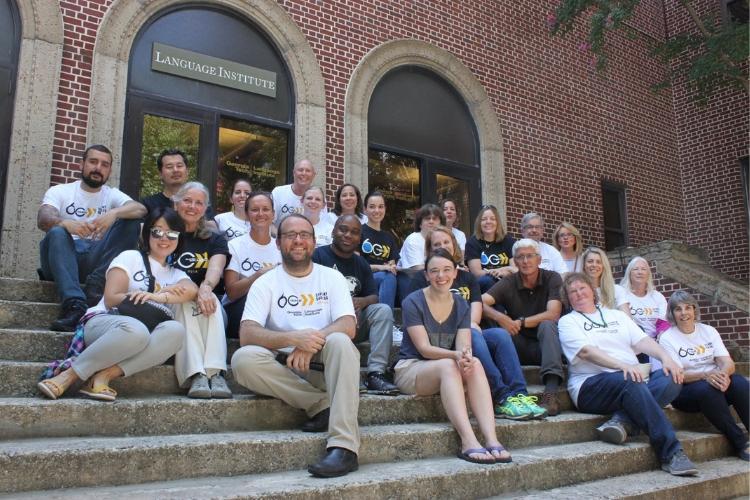 Language Institute instructors sit at steps in front of building wearing 60th anniversary shirts