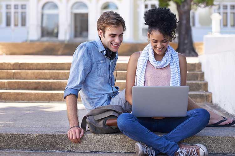 Boy and girl sitting on sidewalk looking at laptop