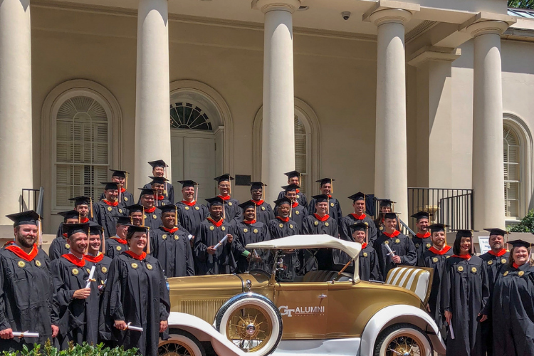 Graduates in caps in gowns standing next to the Ramblin' Wreck