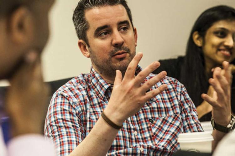 Male learner talking with hands to peers who are intently looking at him