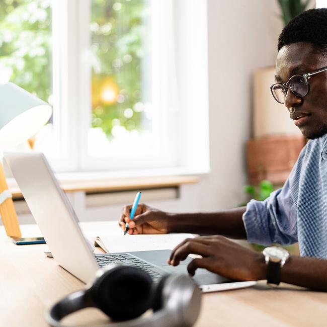 A young African-American man working on a laptop in a home office space.