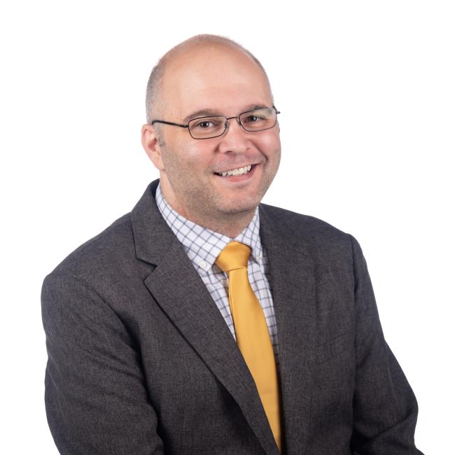 Professional headshot of Peter Graening wearing a black suit jacket and gold tie.