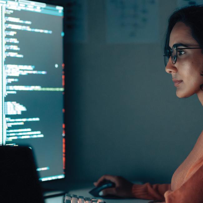 A woman sitting at a desk with multiple monitors.