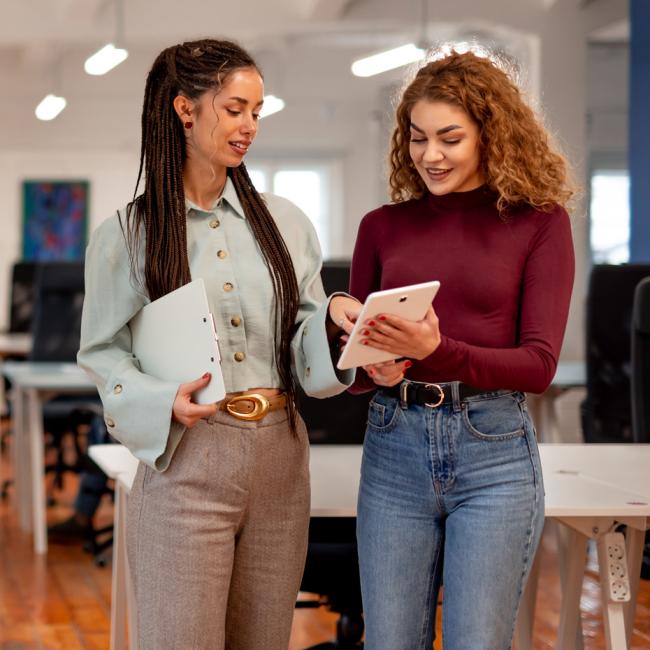 Two colleges walking together in an office discussing topics on a tablet