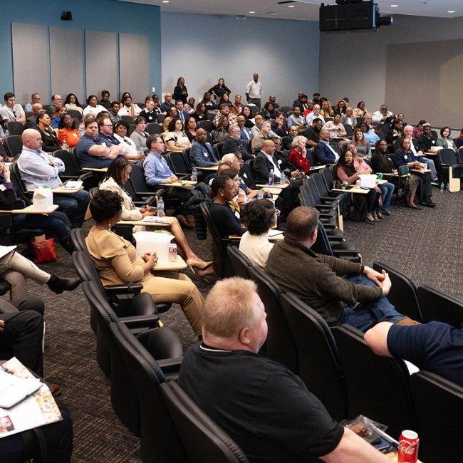 Large group of people listening to a speaker in a conference room.