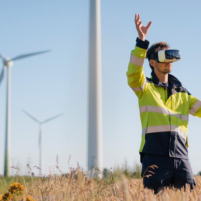 An engineer in a field with windmills wears a VR headset.