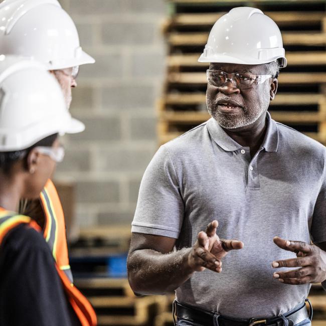 Safety officer in a hard hat speaking with employees in hard hats and other personal protective equipment