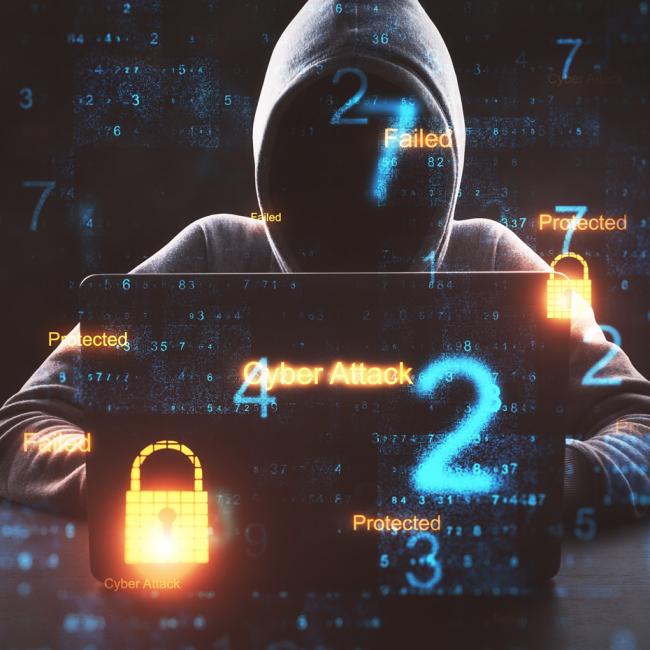 Hacker with laptop sitting in a dark room.