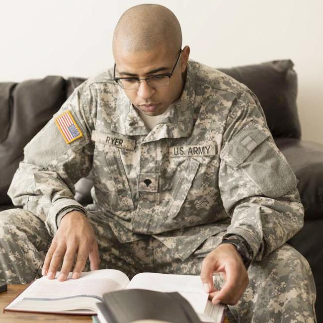 Soldier sitting on couch with books and laptop on table