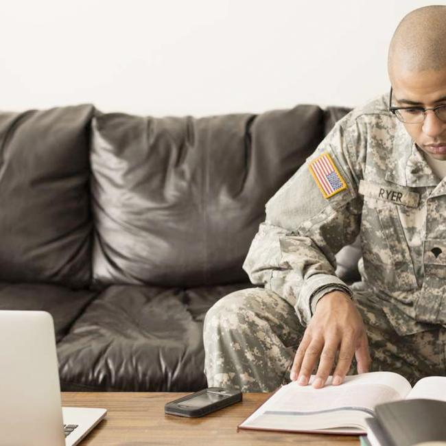 Soldier sitting on couch with books and laptop on table