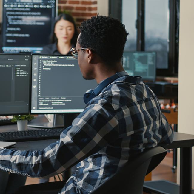 Person sitting at desk with multiple monitors, coding.