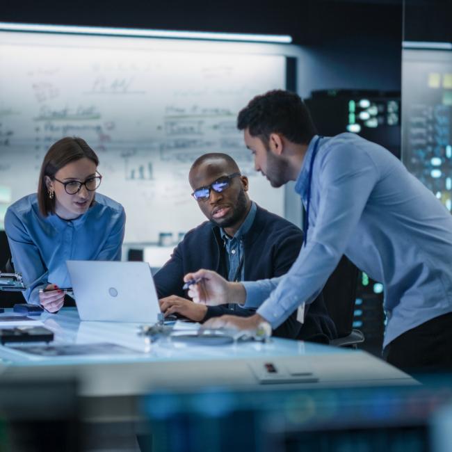 three people sitting at a desk discussing content on a lap top