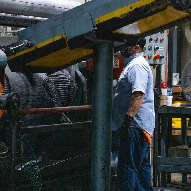 Worker inspecting a large industrial machine with gears and control panels.