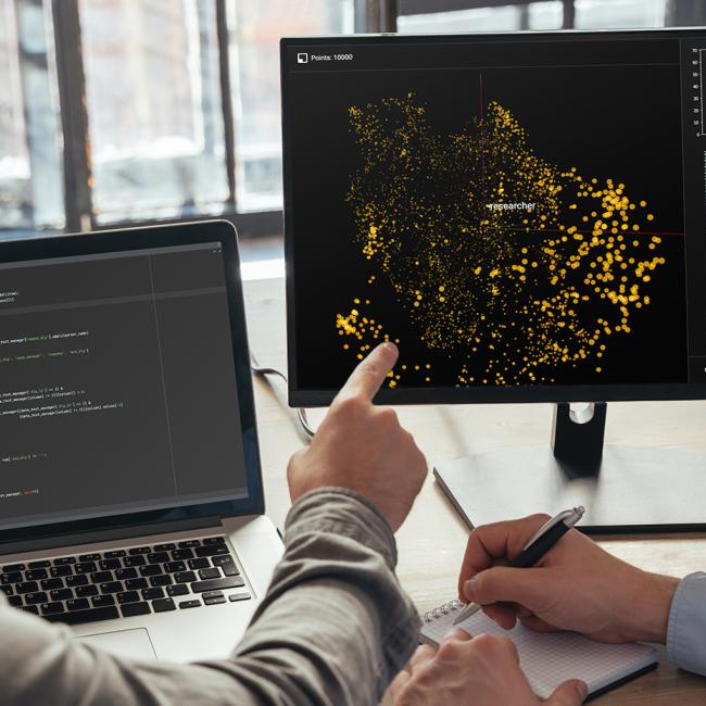 Closeup of two data science specialists looking at two computer screens, analyzing big data.