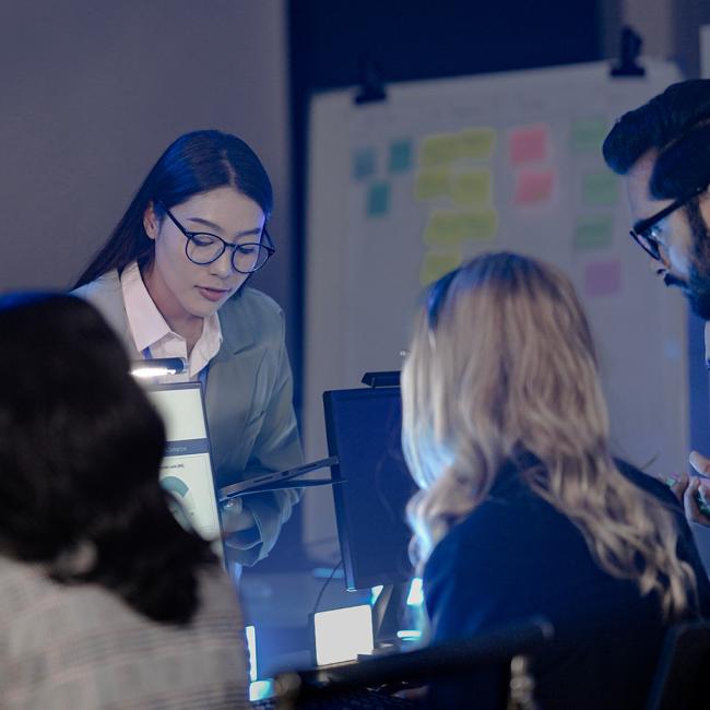 Four people working in an intelligence office viewing screens with reports and world maps