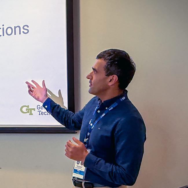 Photograph of a man giving a presentation titled "Securing the Skies: Cybersecurity Challenges and AI-Driven Threats in Drone Operations."