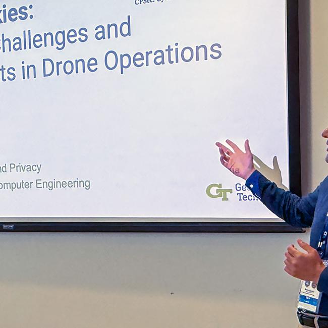 Photograph of a man giving a presentation titled "Securing the Skies: Cybersecurity Challenges and AI-Driven Threats in Drone Operations."