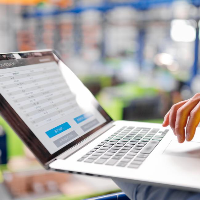 A person wearing a safety vest uses a laptop to review operational data in a manufacturing facility.