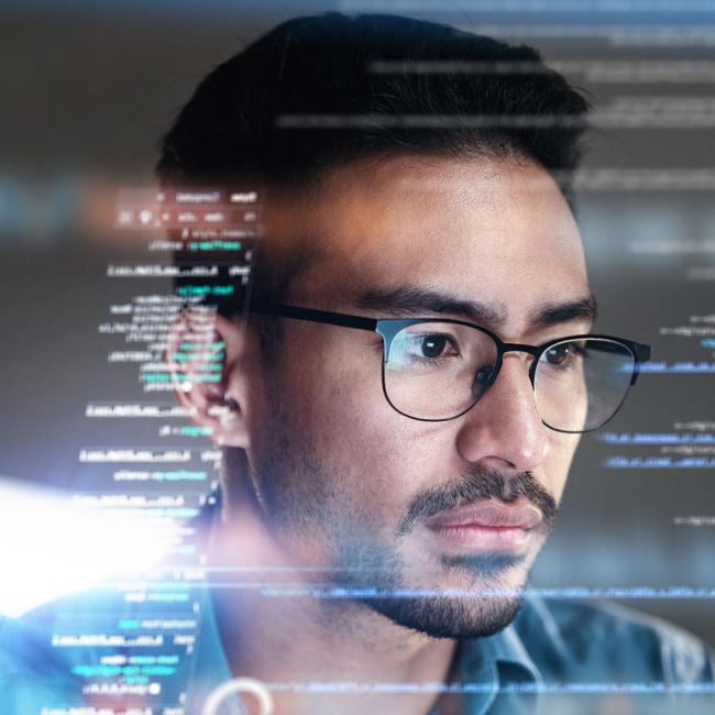A man focused on a transparent screen displaying lines of computer code.