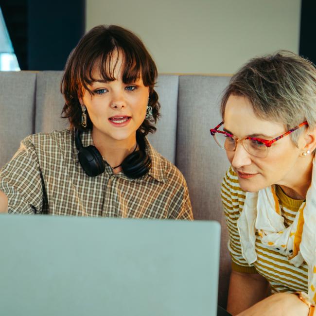 Two colleagues from different generations collaborate around an open laptop in an office.