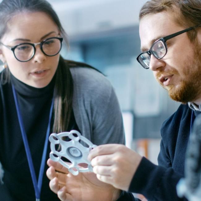 Male and female engineers discussing prototype build with 3D printer.