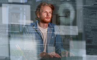 Man sitting at desk looking at floating lines of code and different charts meant to symbolize AI outputs